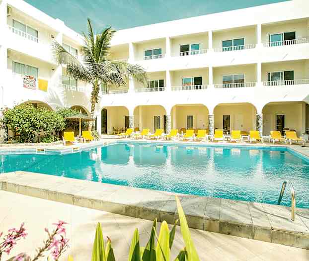 Et utendørsbasseng med gule solsenger og en hvit bygning med balkonger. (AI-generert tekst)