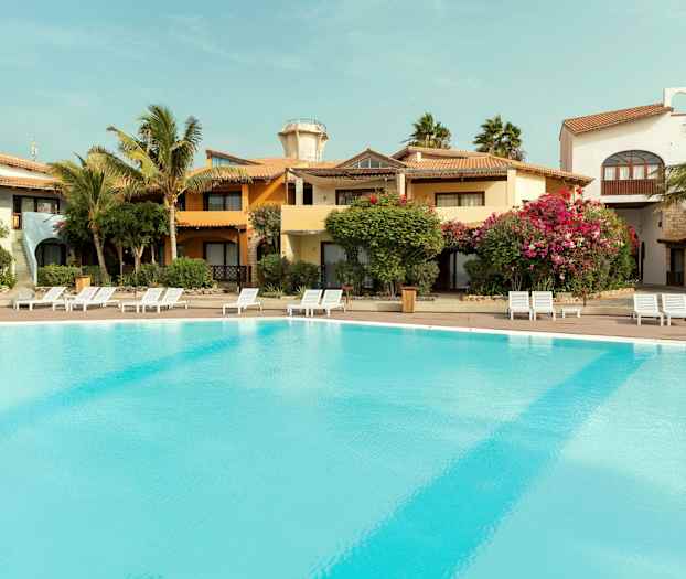 Utendørsbasseng ved ferieanlegg med omkringliggende bygninger og vegetasjon. (AI-generert tekst)