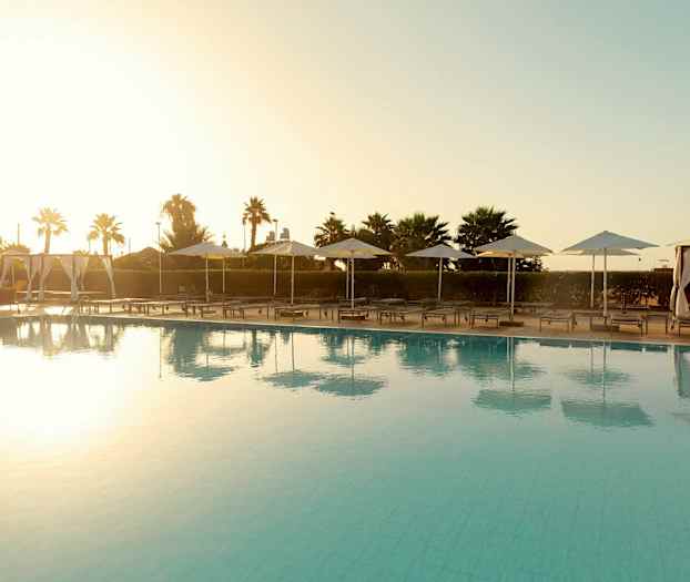 Bassengområde med solsenger og parasoller ved solnedgang. (AI-generert tekst)