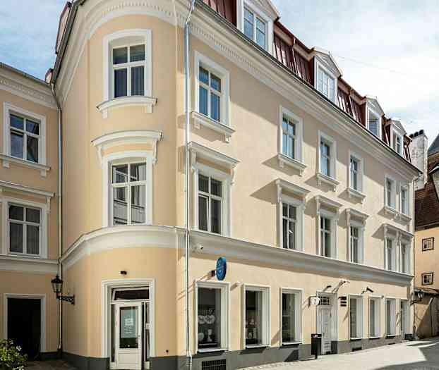 En beige bygning med hvite detaljer og rødt tak i et byområde. (AI-generert tekst)