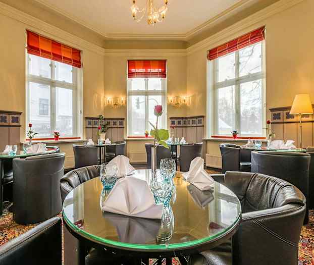 Interiør av en restaurant med dekkede, runde bord og store vinduer. (AI-generert tekst)