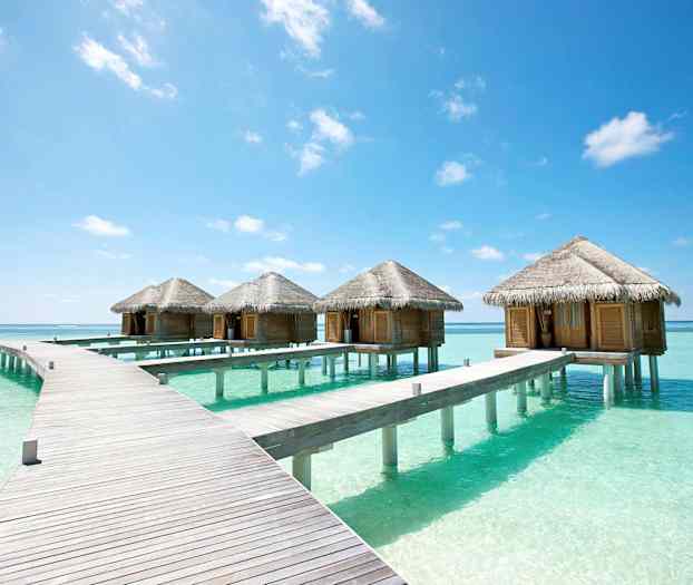 En rekke bungalower på stylter i det klare turkise vannet under en blå himmel. (AI-generert tekst)