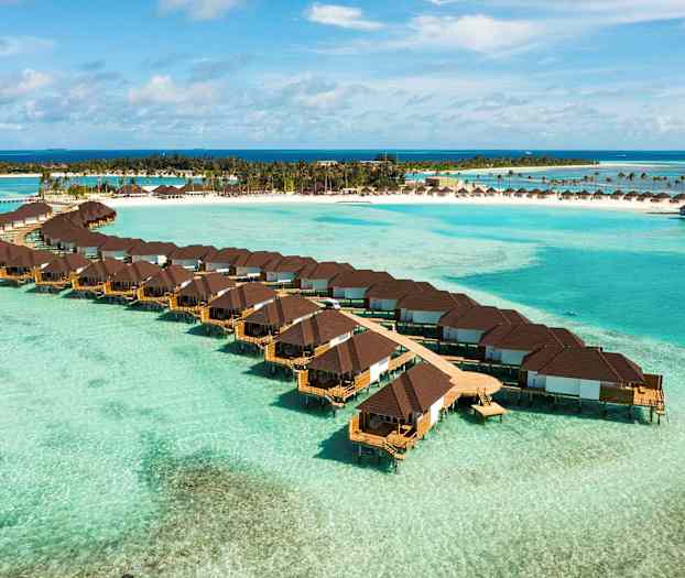 Bungalower over vann med en tropisk strand i bakgrunnen. (AI-generert tekst)