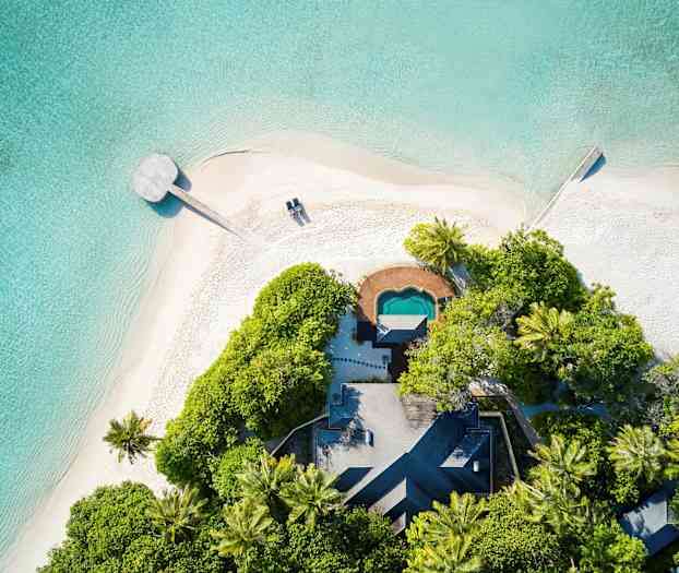 Luftfoto av sandstranden ved det krystallklare tropiske havet, med frodig vegetasjon og en liten bygning. (AI-generert tekst)