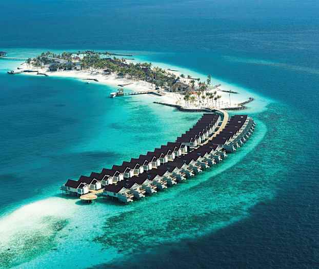 Flyfoto av en øy med strand, palmer og boliger bygget over vann. (AI-generert tekst)