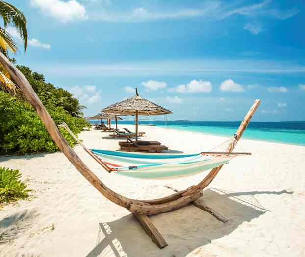 En strand med en hengekøye, parasoller og solsenger ved havet. (AI-generert tekst)