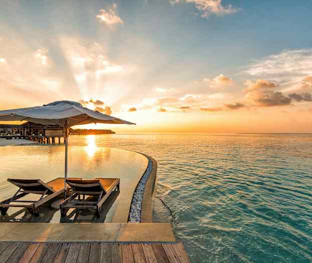 To solsenger med parasoll ved et evighetsbasseng og havet i solnedgang. (AI-generert tekst)