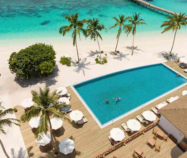 Utsikt over et bassengområde med solsenger på en tropisk strand, omgitt av palmer og krystallklart vann. (AI-generert tekst)