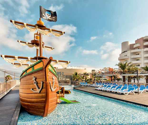 Bilde av bassengområdet med et leke-piratskip og solsenger i bakgrunnen. (AI-generert tekst)