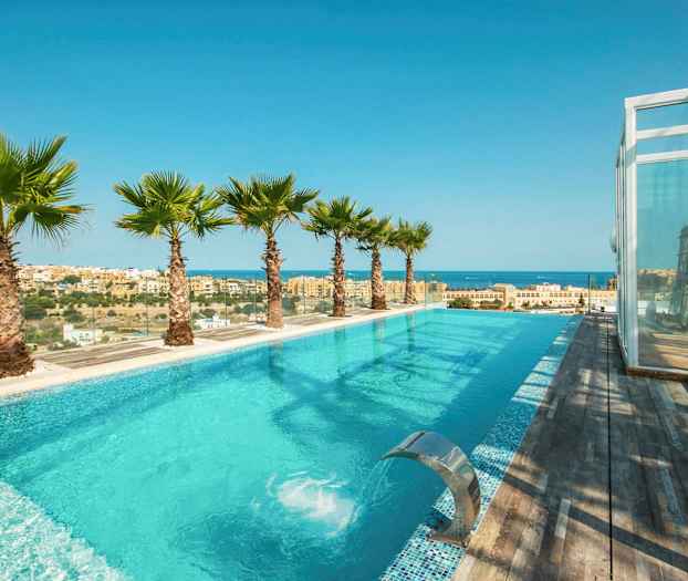 Et infinitybasseng med utsikt over havet og byen, omgitt av palmer og tredekke. (AI-generert tekst)