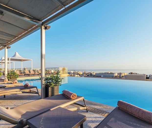 Solstoler ved et infinitybasseng med utsikt over en by og havet. (AI-generert tekst)