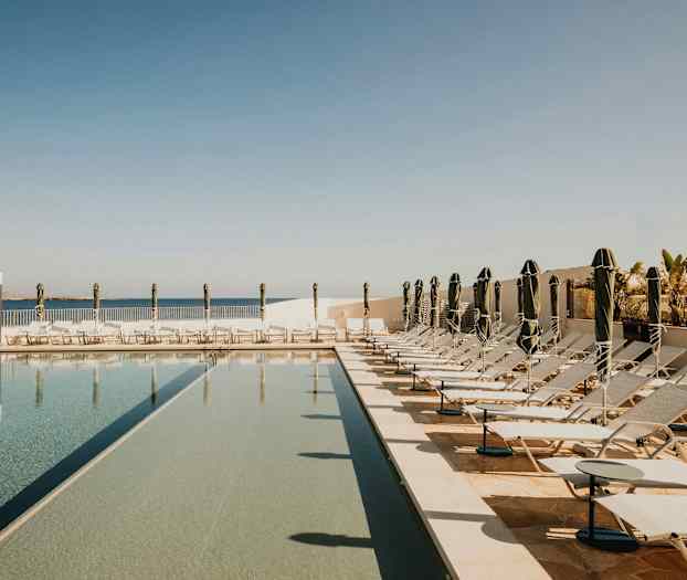 Bilde av et basseng med solsenger og parasoller i et solrikt utendørsområde. (AI-generert tekst)