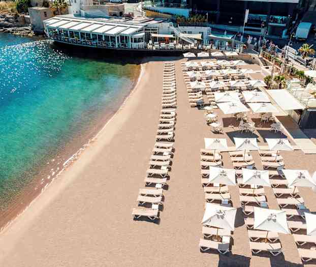 Strand med solsenger og parasoller samt en nærliggende bygning. (AI-generert tekst)