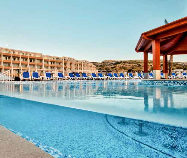 Utendørs svømmebasseng med solsenger og hotellbygning i bakgrunnen. (AI-generert tekst)