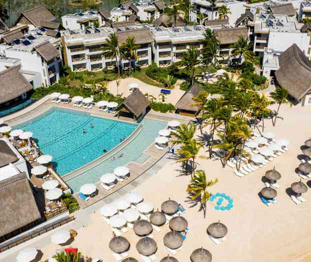 Flyutsikt over et hotellområde med basseng, grøntområder og parasoller på en sandstrand. (AI-generert tekst)