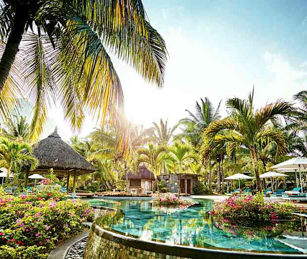 Et basseng omgitt av palmer og vegetasjon i et tropisk område. (AI-generert tekst)