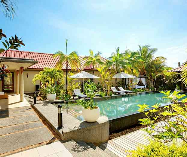 Et åpent miljø med et basseng omgitt av solsenger og parasoller, med grønt og bygninger i bakgrunnen. (AI-generert tekst)