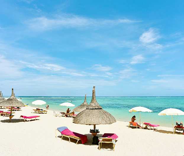 En strand med parasoller og solsenger ved havet. (AI-generert tekst)