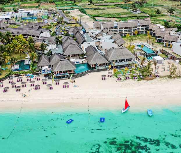 Luftfoto av en strand med solsenger, parasoller og en resort ved vannkanten. (AI-generert tekst)