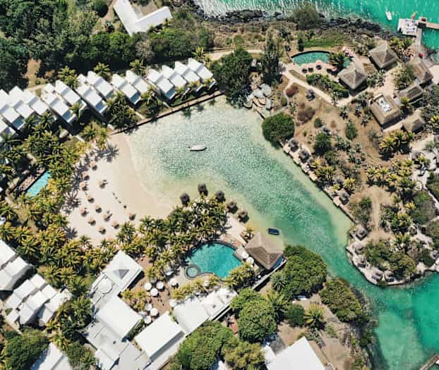 Flyfoto av ett hotellområde med basseng, en sandstrand og vegetasjon ved vannet. (AI-generert tekst)