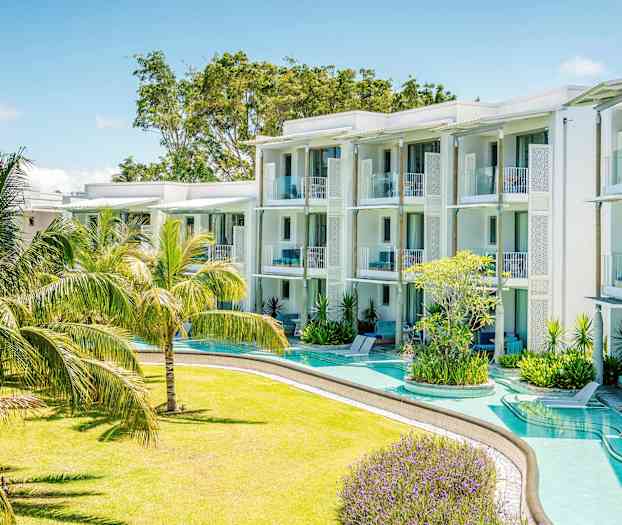 Et moderne feriehotell med hvite bygninger og balkonger omgitt av en frodig hage med tropiske planter. (AI-generert tekst)