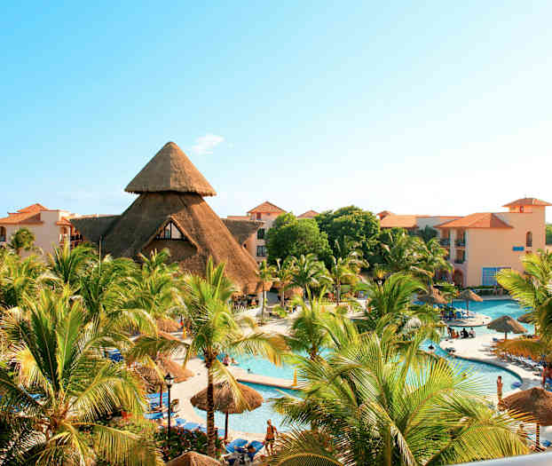 En feriested med basseng, palmer og bygninger med runde stråtak. (AI-generert tekst)