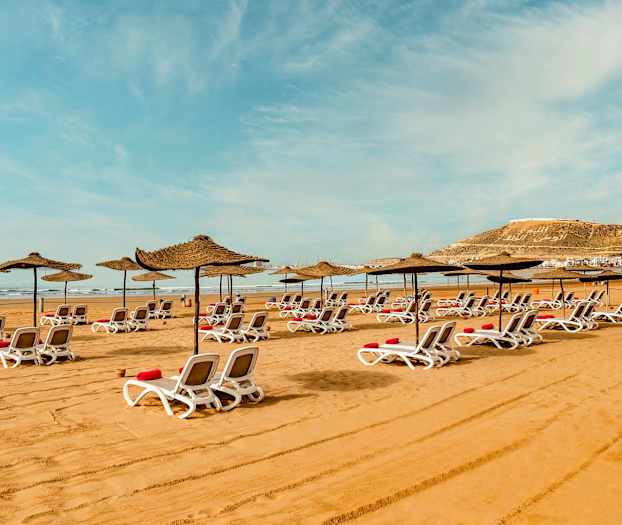 Solstoler med parasoller på sandstrand. (AI-generert tekst)