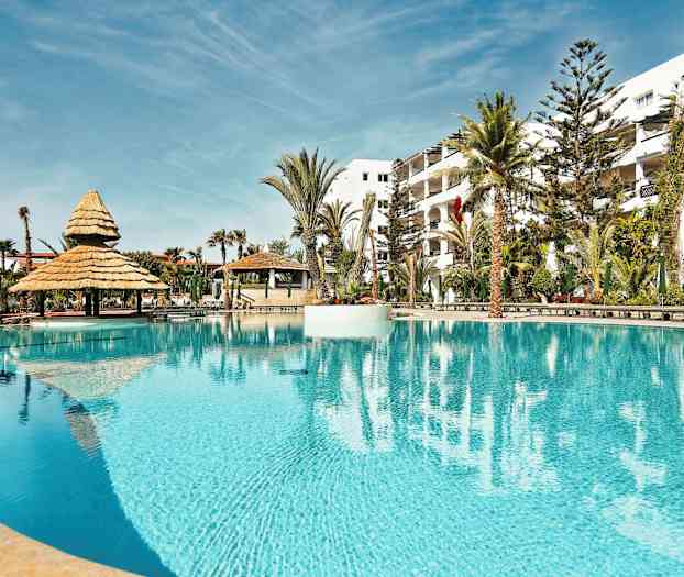 Et basseng med parasoller og omgivelser av palmer. (AI-generert tekst)