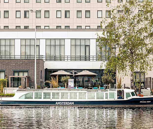 Bilde av en kanalbåt foran en bygning ved vannet. (AI-generert tekst)