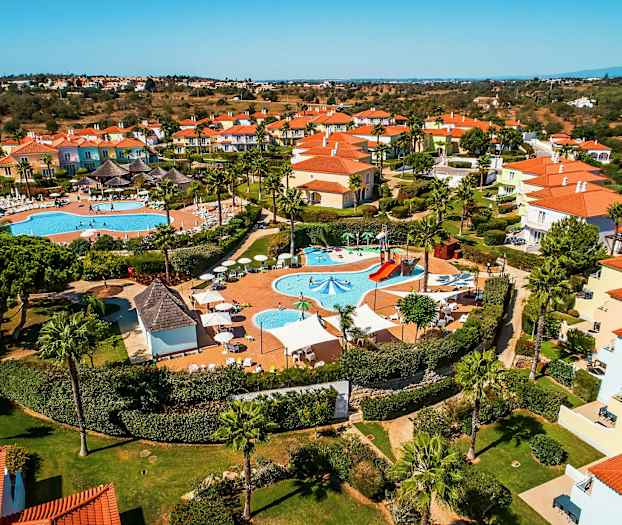 Flyfoto av et feriekompleks med bassenger og fargerike hus. (AI-generert tekst)