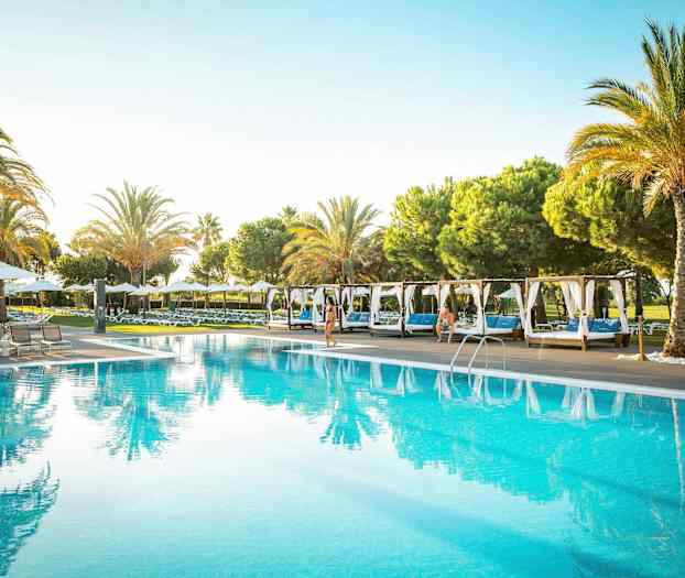 Et utendørsbasseng omgitt av solsenger og palmer. (AI-generert tekst)