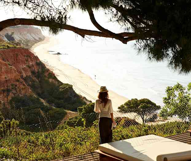 Kvinnen står ved kanten med utsikt over en sandstrand og klippeformasjoner. (AI-generert tekst)