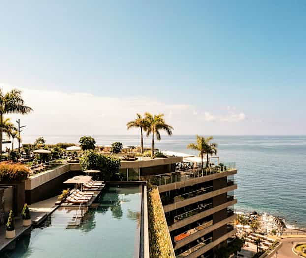 En utsikt over et hotellområde ved havet, med bassenger og palmer. (AI-generert tekst)