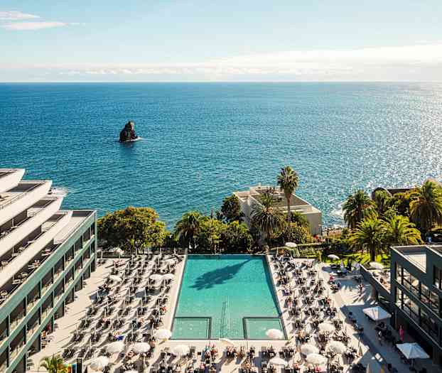 Hotell ved sjøen med basseng og solsenger. (AI-generert tekst)