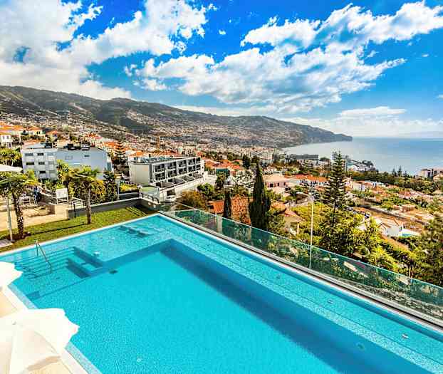 Utsikt over et basseng med omkringliggende bygninger og havet i bakgrunnen. (AI-generert tekst)