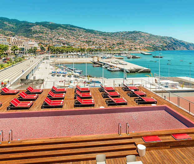 Bassengområde med solsenger og utsikt over havn og by. (AI-generert tekst)