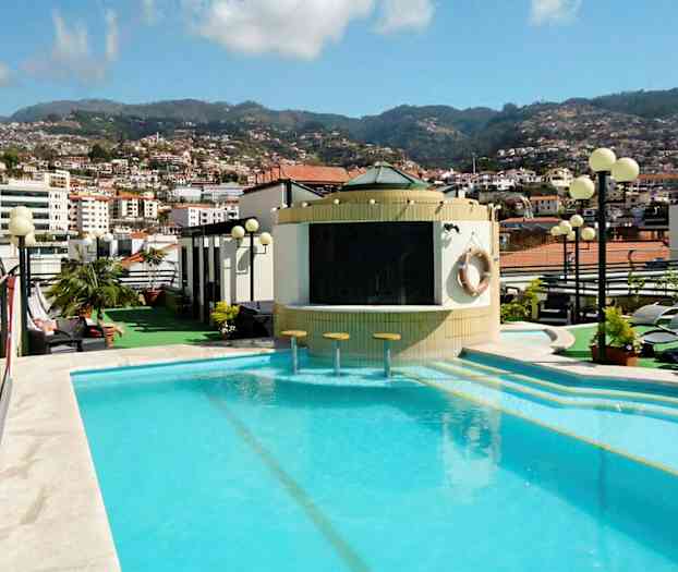 Et utendørsbasseng på et hotell med utsikt over byen og fjellene i bakgrunnen. (AI-generert tekst)