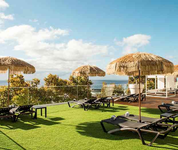 Solstoler med håndklær og parasoller på en plen med utsikt mot havet. (AI-generert tekst)