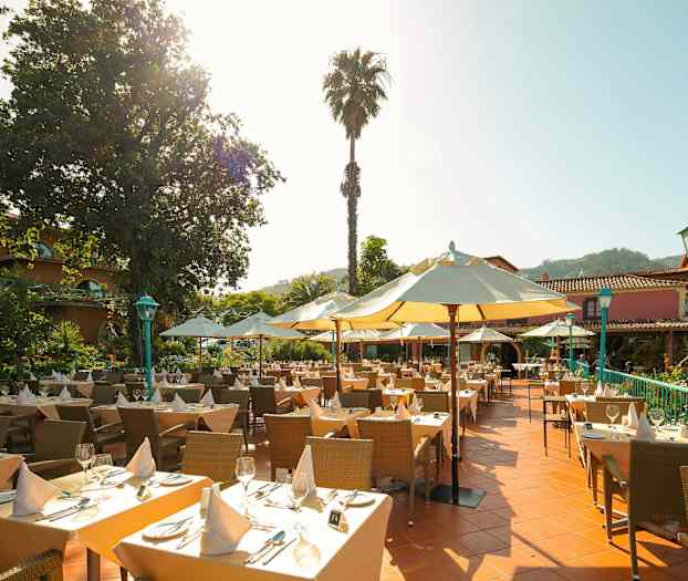 Uteservering med dekkede bord, parasoller og en frodig omgivelse. (AI-generert tekst)