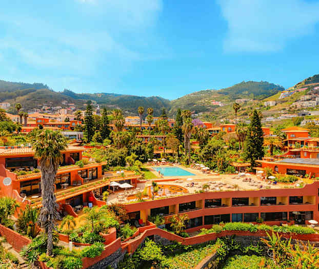 Et anlegg med terrakottafargede bygninger, basseng og frodig vegetasjon, plassert i en dal omgitt av åser. (AI-generert tekst)