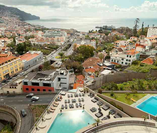 Utsikt over en by med bygninger, veier, to bassenger og havet i bakgrunnen. (AI-generert tekst)