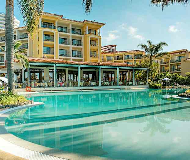 Hotellfasade ved et stort basseng omgitt av palmer. (AI-generert tekst)