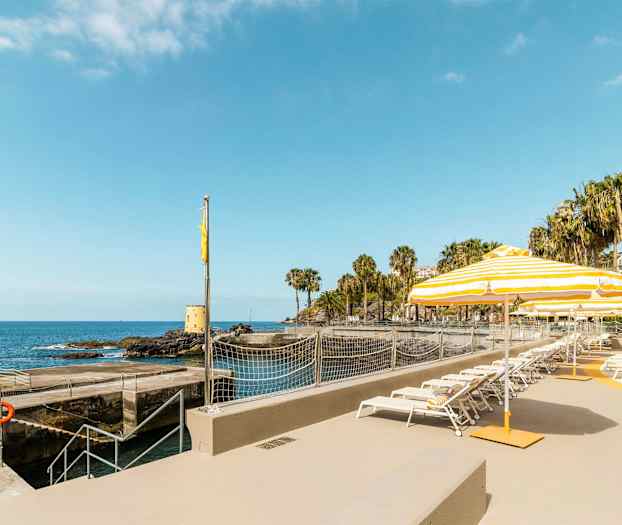 Solstoler og parasoller ved en kystnær beliggenhet med havutsikt. (AI-generert tekst)