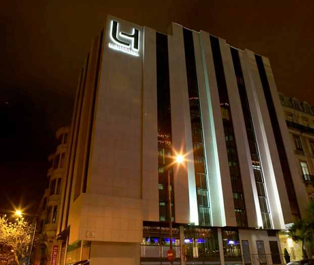 Et hotell med moderne ytre fotografert om natten. Bygningens fasade er belyst. (AI-generert tekst)