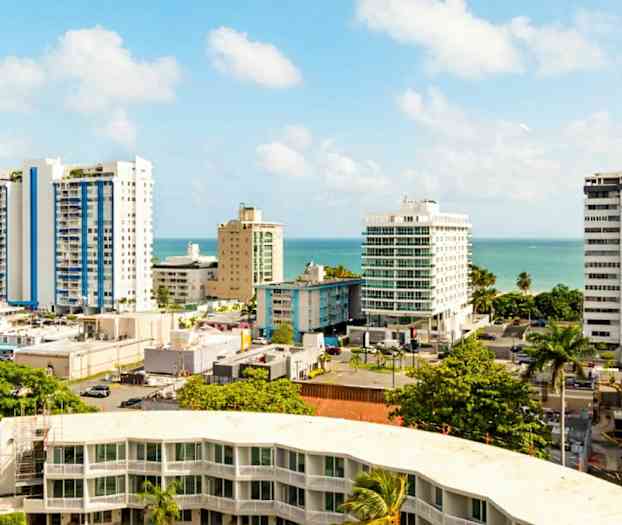 Byutsikt med høyhus og palmer nær havet under en klar blå himmel. (AI-generert tekst)