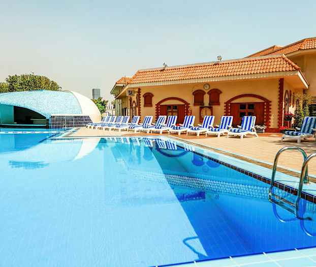 Et svømmebasseng ved et hotell med solsenger og en bar i bakgrunnen. (AI-generert tekst)