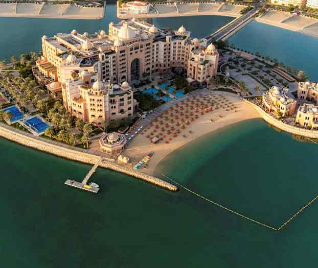 Luftfoto av et luksuriøst hotellkompleks ved en strand med solsenger og parasoller, omgitt av vann. (AI-generert tekst)