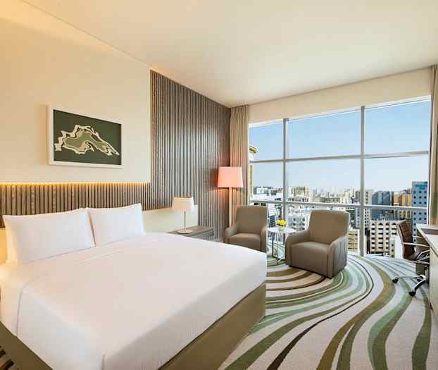 Et moderne hotellrom med en stor seng og to stoler foran et vindu. (AI-generert tekst)