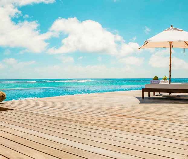 Solstoler og parasoll på en terrasse ved sjøen. (AI-generert tekst)