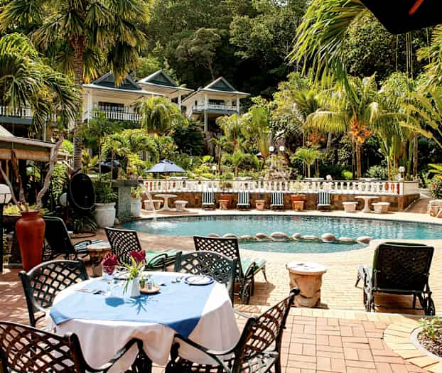 Et utendørsbasseng omgitt av palmer og vegetasjon med en møblert sittegruppe nær vannet. (AI-generert tekst)